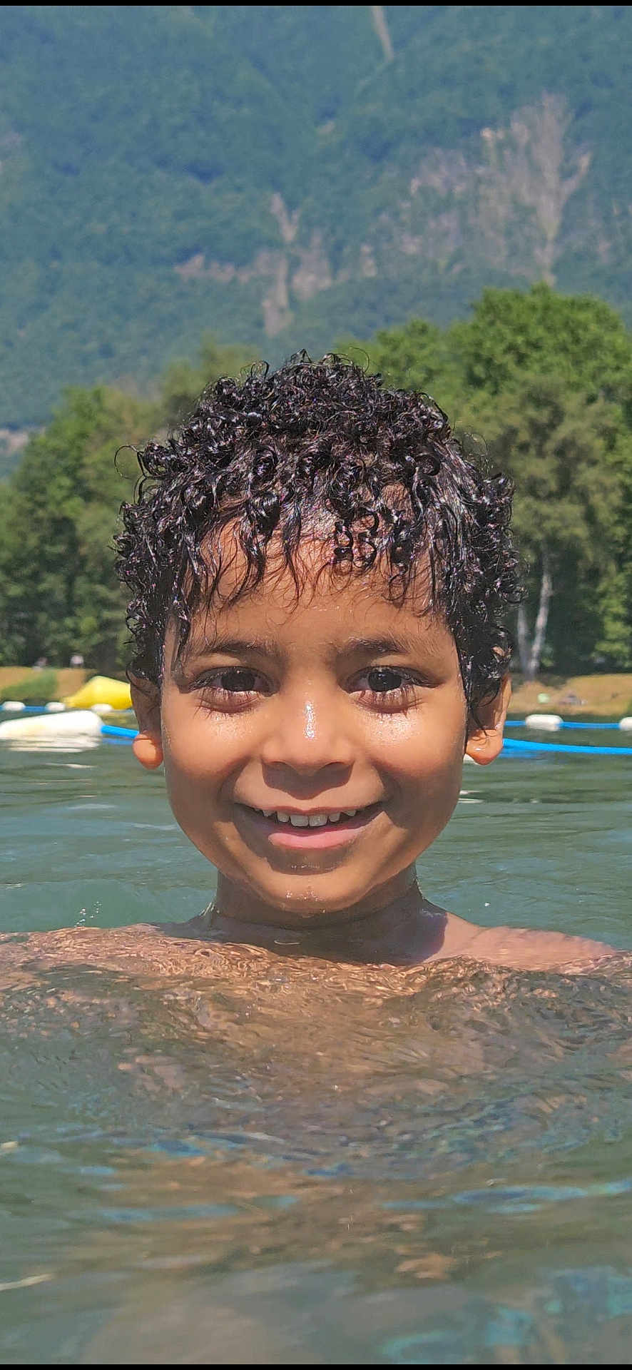 Kaïs participe au concours pour gagner de l'argent avec cette photo : child, boy, smile, water, lake, swimming, curly_hair, outdoor, nature, trees, mountains, summer, sunlight, happy, face, head, person, recreation, holiday, leisure