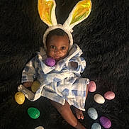 Aiden is registered to the contest to win money with this photo: baby, balloon, bonnet, cap, clothing, coat, costume, doll, egg, face, food, hat, head, person, photography, portrait, purple, sitting, sweets, toy
