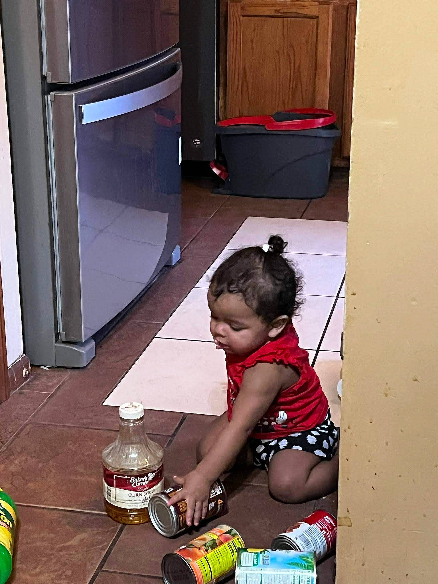 Carolina is registered to the contest to win money with this photo: audio_equipment, child, drink, floor, flooring, fun, green, human_leg, machine, person, plastic_bottle, play, refrigerator, room, sitting, toddler, water_bottle