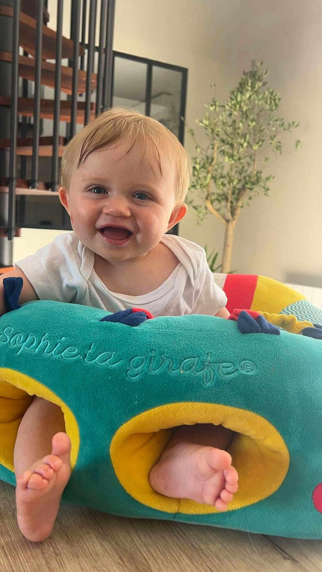 Naoh participe au concours pour gagner de l'argent avec cette photo : baby, smiling, toy, colorful, indoor, wooden_floor, plant, spiral_staircase, face, feet, child, white_clothing, happy, home, furniture, soft_toy, playful, infant, cute, portrait