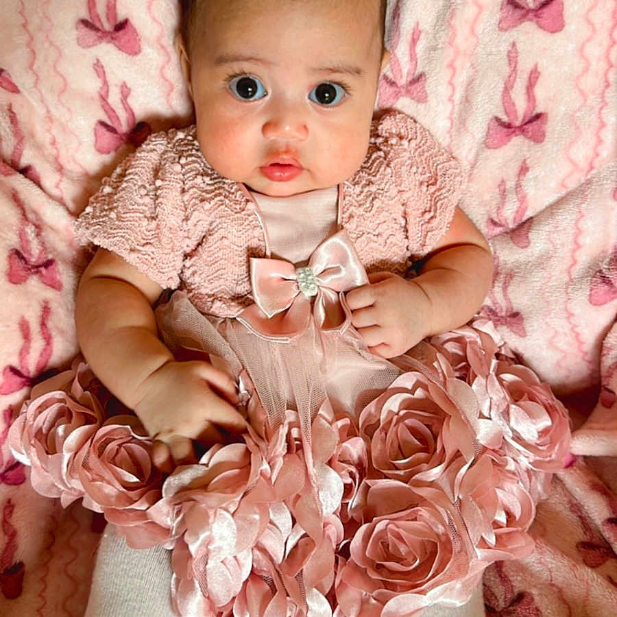 Malia is registered to the contest to win money with this photo: baby, infant, pink_dress, fabric_roses, blanket, bows, white_shoes, tights, cute, wide_eyes, portrait, child, indoors, soft_texture, clothing, adorable, fashion, laying_down, young_child, headband