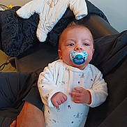 Aylane participe au concours pour gagner de l'argent avec cette photo : baby, infant, child, pacifier, onesie, adult_hand, blanket, jacket, couch, clothing, portrait, indoor, furniture, sitting, cute, sleepy, looking_up, printed_onesie, holding, skin_tone