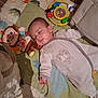 baby, infant, sleeping, play_mat, dinosaur_pattern, plush_monkey, soft_toy, rattle, onesie, blanket, face, closed_eyes, hand, nursery, pillow, floor, indoors, toy_ring, peaceful, bedtime