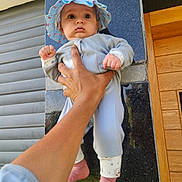 Yassine is registered to the contest to win money with this photo: baby, child, hand, hat, blue_hat, infant, clothing, foot, barefoot, person, wall, tiles, wooden_door, outdoor, holding, portrait, cute, expression, skin, fingers