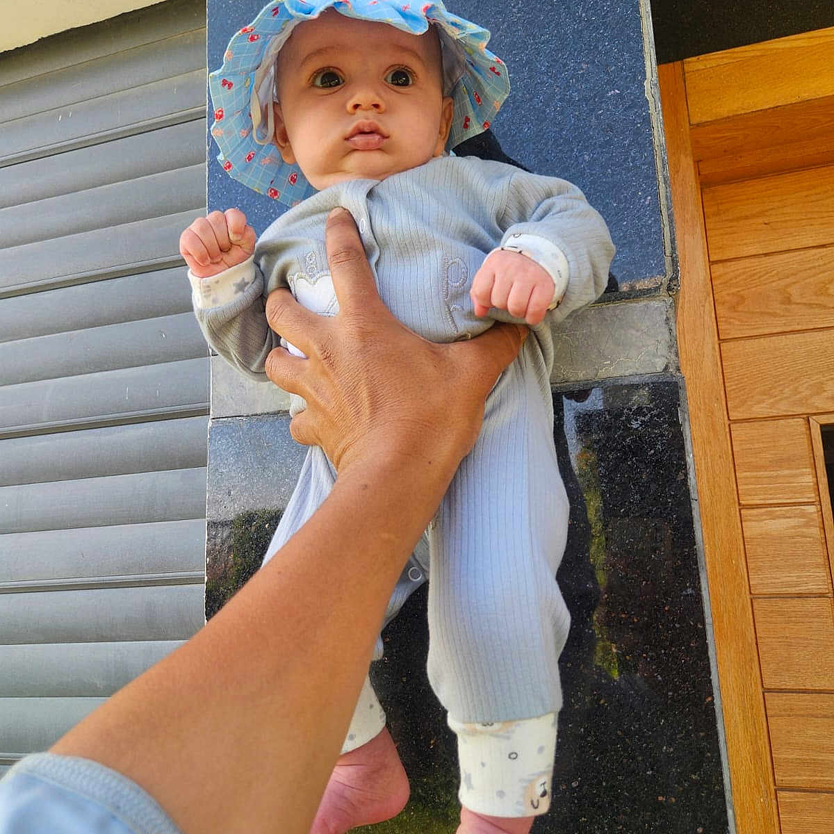 Yassine is registered to the contest to win money with this photo: baby, barefoot, blue_hat, child, clothing, cute, expression, fingers, foot, hand, hat, holding, infant, outdoor, person, portrait, skin, tiles, wall, wooden_door