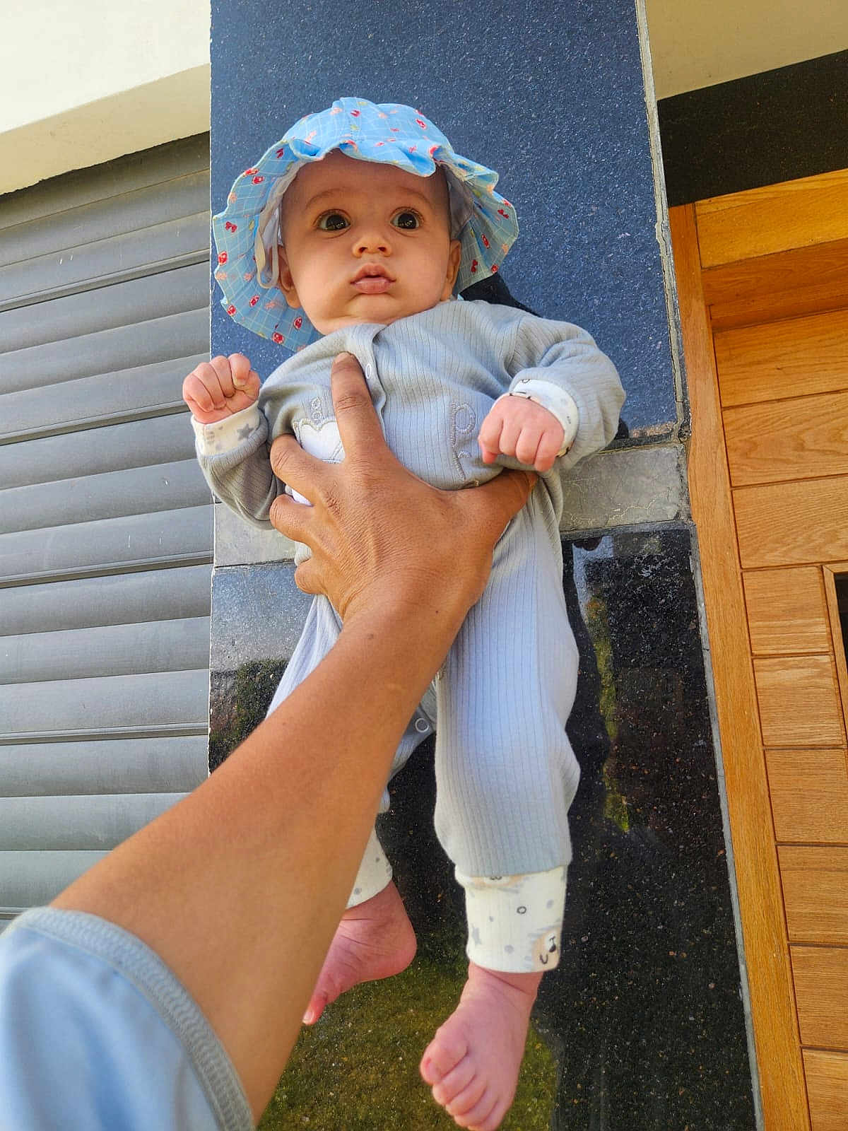 Yassine is registered to the contest to win money with this photo: baby, child, hand, hat, blue_hat, infant, clothing, foot, barefoot, person, wall, tiles, wooden_door, outdoor, holding, portrait, cute, expression, skin, fingers