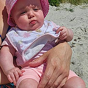 Ashley participe au concours pour gagner de l'argent avec cette photo : baby, child, pink_hat, bib, beach, sand, sunlight, adult_hand, outdoor, summer, nature, grass, blue_sky, portrait, cute, infant, skin, clothing, person, holding