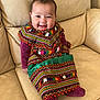 baby, smiling, child, traditional_clothing, colorful, sitting, couch, leather, indoors, portrait, happy, cute, patterned_dress, infant, young_child, cozy, fabric, face, person, warm