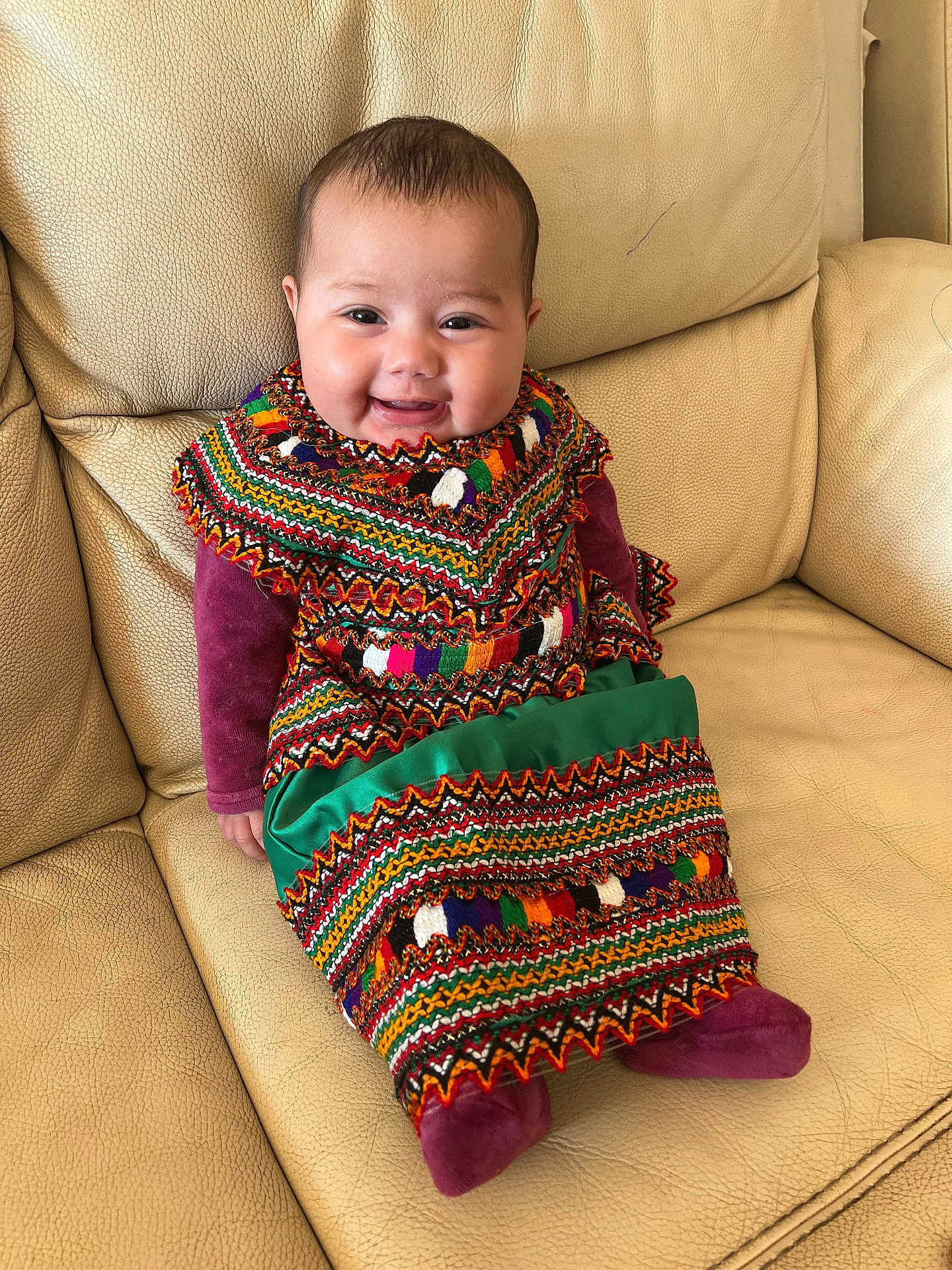 Hannah participe au concours pour gagner de l'argent avec cette photo : baby, smiling, child, traditional_clothing, colorful, sitting, couch, leather, indoors, portrait, happy, cute, patterned_dress, infant, young_child, cozy, fabric, face, person, warm