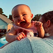 Kamdyn is registered to the contest to win money with this photo: baby, child, person, smiling, happy, outdoor, daylight, holding, shoulder, clothing, striped, earring, woman, head, face, sky, house, tree, pool, sunlight