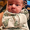 baby, infant, blanket, dinosaur_pattern, face, eyes, hand, watch, clothing, furniture, footwear, person, indoor, portrait, expression, skin, head, sitting, holding, casual