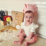 Solomia participe au concours pour gagner de l'argent avec cette photo : baby, infant, paper_crown, kitchen_counter, flour, rolling_pin, cutting_board, flowers, knife_block, white_wall_tiles, celebration, 5_months, surprised_expression, cute, sitting, cooking, home, child, portrait, kitchen