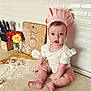 baby, infant, paper_crown, kitchen_counter, flour, rolling_pin, cutting_board, flowers, knife_block, white_wall_tiles, celebration, 5_months, surprised_expression, cute, sitting, cooking, home, child, portrait, kitchen