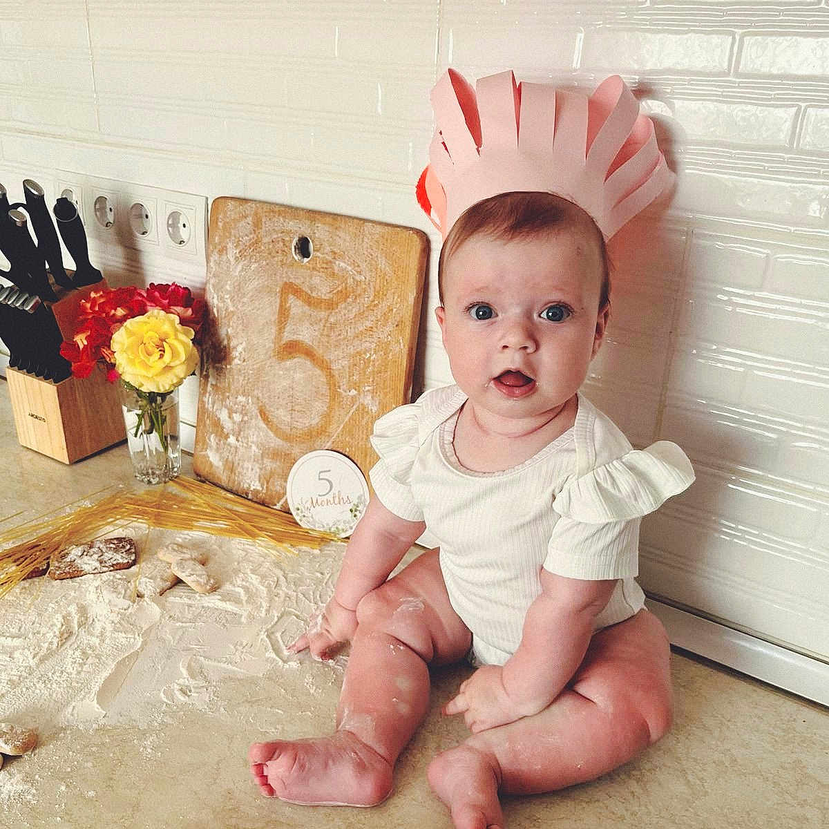 Solomia participe au concours pour gagner de l'argent avec cette photo : 5_months, baby, celebration, child, cooking, cute, cutting_board, flour, flowers, home, infant, kitchen, kitchen_counter, knife_block, paper_crown, portrait, rolling_pin, sitting, surprised_expression, white_wall_tiles