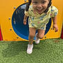 child, girl, smiling, playground, tunnel, yellow_clothing, pink_shoes, grass, outdoor, happy, curly_hair, pigtails, running, fun, play, daylight, colorful, casual_wear, active, person