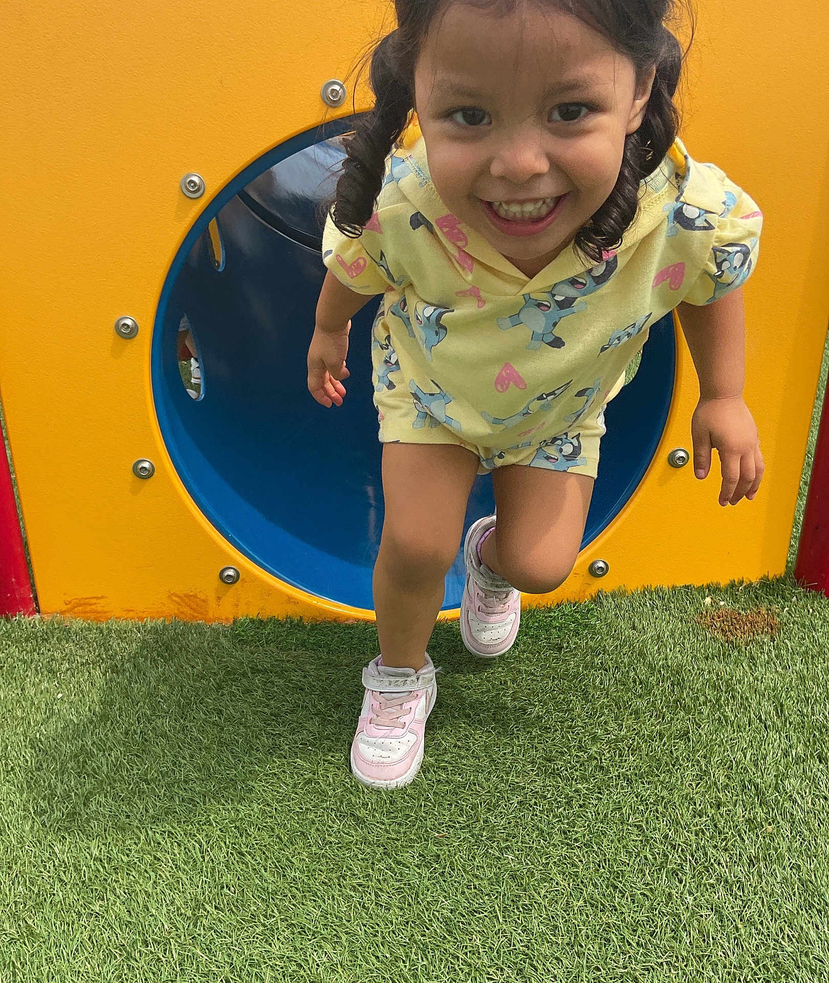 Mia joined the competition — help win amazing prizes! child, girl, smiling, playground, tunnel, yellow_clothing, pink_shoes, grass, outdoor, happy, curly_hair, pigtails, running, fun, play, daylight, colorful, casual_wear, active, person