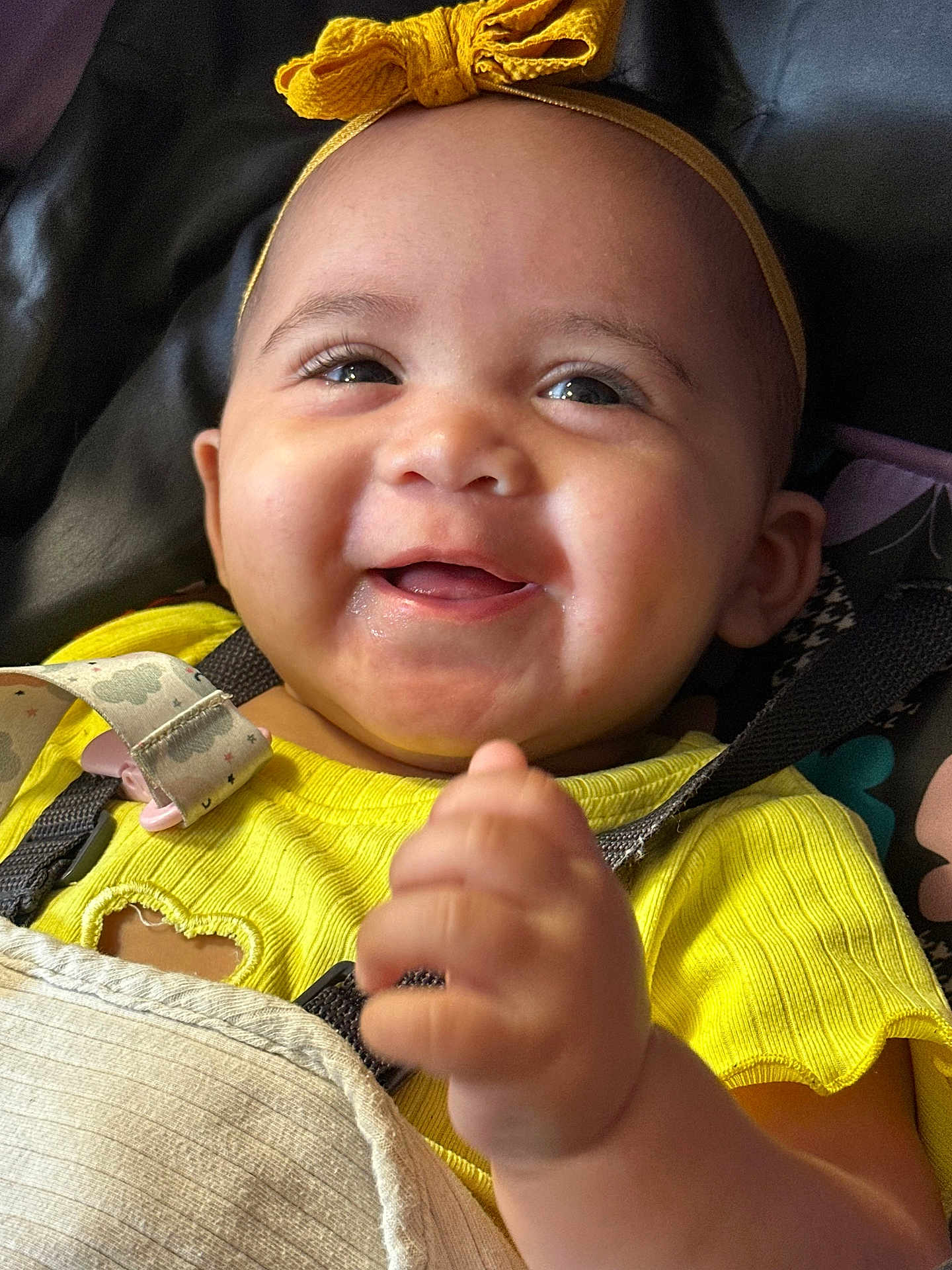 Jewelyah is registered to the contest to win money with this photo: baby, smiling, yellow_headband, yellow_clothing, infant, happy, closeup, face, hand, cute, child, portrait, seatbelt, car_seat, expression, indoors, skin, headwear, young_child, emotion