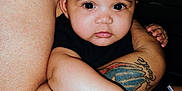 Jewelyah is registered to the contest to win money with this photo: baby, child, infant, tattoo, arm, skin, person, holding, closeup, face, eyes, cute, indoors, black_clothing, human, portrait, expression, love, family, bond