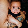 baby, child, infant, tattoo, arm, skin, person, holding, closeup, face, eyes, cute, indoors, black_clothing, human, portrait, expression, love, family, bond