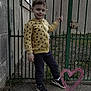 Raphaël participe au concours pour gagner de l'argent avec cette photo : child, smiling, yellow_hoodie, mickey_mouse_pattern, green_gate, outdoor, concrete_ground, stone_wall, casual_pose, black_shoes, pants, young_boy, happy, fence, grass, lock, playful_doodle, heart, daylight, person