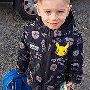Raphaël participe au concours pour gagner de l'argent avec cette photo : child, boy, smiling, outdoor, gravel, car, black_car, jacket, pokemon, pikachu, backpack, toy, pacifier, shoes, clothing, face, hair, person, standing, casual