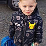 child, boy, smiling, outdoor, gravel, car, black_car, jacket, pokemon, pikachu, backpack, toy, pacifier, shoes, clothing, face, hair, person, standing, casual