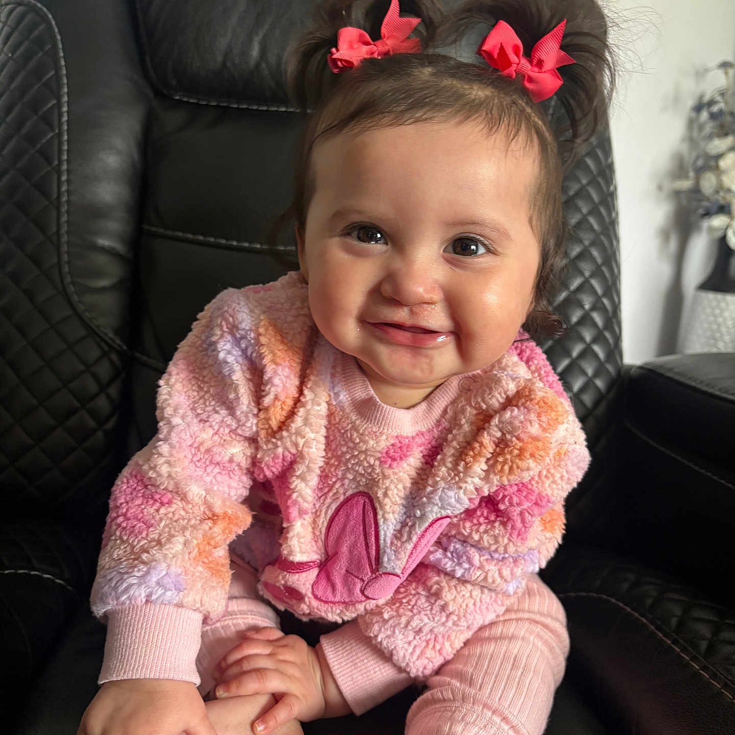 Maily is registered to the contest to win money with this photo: baby, child, smile, pink_bows, sweater, fuzzy_clothing, sitting, black_leather_chair, happy, cute, indoors, portrait, infant, hands, feet, person, young_child, cozy, warm_clothing, playful