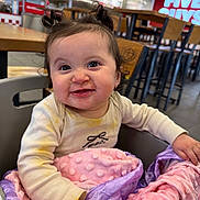 Maily is registered to the contest to win money with this photo: baby, child, smiling, high_chair, blanket, indoor, restaurant, fast_food, hair_pigtails, clothing, face, happy, messy, table, chair, person, food, cute, expression, portrait