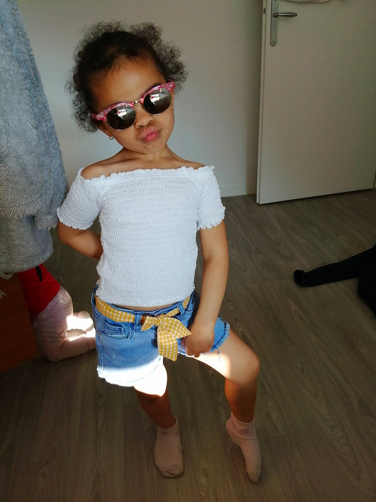 Kinzah participe au concours pour gagner de l'argent avec cette photo : baby_toddler_clothing, eyewear, fashion_design, floor, flooring, glasses, goggles, hairstyle, hardwood, joint, knee, person, sandal, shoe, sleeve, standing, sunglasses, thigh, vision_care, waist