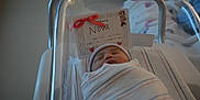 Nova is registered to the contest to win money with this photo: newborn, baby, hospital, bassinet, blanket, swaddled, sleeping, infant, hat, name_card, nursery, mickey_mouse, minnie_mouse, cute, peaceful, indoor, person, face, child, medical_equipment