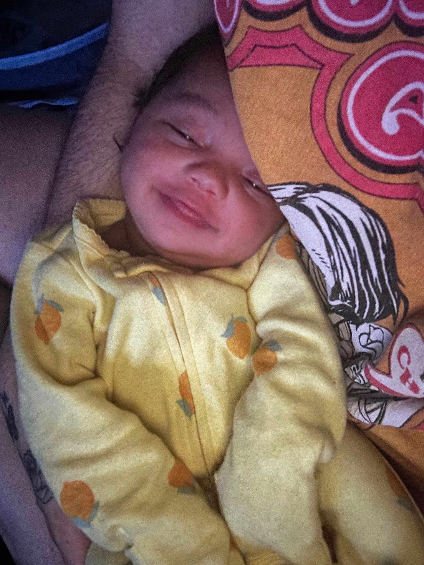Nova is registered to the contest to win money with this photo: baby, child, yellow_onesie, orange_prints, smile, face, person, adult, tattoo, graphic_tshirt, close_up, cozy, indoor, comfort, snuggle, warm_lighting, portrait, cute, happy, sleepy