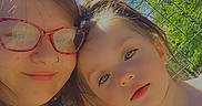 Sylvia is registered to the contest to win money with this photo: woman, child, outdoor, selfie, glasses, smile, sunlight, trees, blue_sky, fence, tattoo, tank_top, lanyard, face, pink_heart, affection, nature, portrait, summer, happy