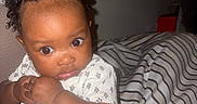 Star is registered to the contest to win money with this photo: baby, child, cozy, curly_hair, cute, expression, face, hand, holding, indoor, infant, person, portrait, seated, skin, soft_light, striped_blanket, white_clothing, wide_eyes, young