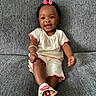 Star is registered to the contest to win money with this photo: accessory, baby, child, clothing, comfortable, couch, cute, footwear, gray_couch, happy, home, indoors, infant, person, pink_bow, portrait, sandals, sitting, smiling, white_outfit