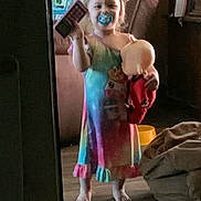 Memphys is registered to the contest to win money with this photo: child, toddler, barefoot, dress, colorful_clothing, pacifier, doll, toy, indoor, living_room, furniture, blanket, floor, window, smile, person, home, cozy, play, young_child