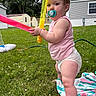 toddler, child, grass, outdoor, pacifier, toy, water_toy, pink_shirt, diaper, blanket, summer, backyard, greenery, hose, mobile_home, playing, barefoot, daytime, nature, cute