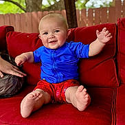 Jaxon is registered to the contest to win money with this photo: baby, child, smiling, red_couch, blue_shirt, red_shorts, barefoot, outdoor, fence, tree, person, sitting, happy, cute, infant, portrait, hand, foot, skin, cushion