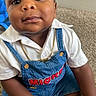 Jahmare is registered to the contest to win money with this photo: baby, child, indoor, sitting, carpet, clothing, overalls, white_shirt, gold_chain, face, expression, person, cute, portrait, skin, hand, foot, young_child, curious, casual