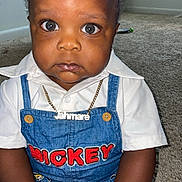 Jahmare joined the competition — help win amazing prizes! toddler, child, baby, overalls, denim, white_shirt, necklace, nameplate, carpet, indoor, floor, person, cute, serious_expression, big_eyes, hair_tied, room, window, toy, mickey