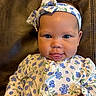 Everlee is registered to the contest to win money with this photo: baby, infant, child, face, headband, tongue, clothing, floral_pattern, blue, white, hand, sitting, portrait, cute, expression, leather, background, person, young_child, indoors