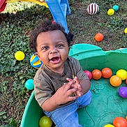 Messiah joined the competition — help win amazing prizes! toddler, child, smiling, outdoor, grass, plastic_container, colorful_balls, playground_slide, curly_hair, happy, casual_clothing, jeans, short_sleeve_shirt, play, fun, daylight, greenery, fence, toy, nature