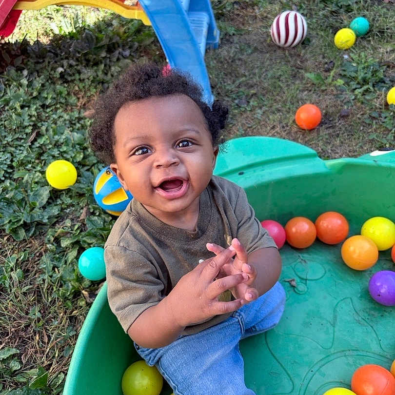Messiah joined the competition — help win amazing prizes! casual_clothing, child, colorful_balls, curly_hair, daylight, fence, fun, grass, greenery, happy, jeans, nature, outdoor, plastic_container, play, playground_slide, short_sleeve_shirt, smiling, toddler, toy