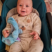 Thyméo a rejoint le concours — aidez-le/la à gagner de superbes lots ! baby, infant, smiling, plush_toy, onesie, cushion, blue_seat, happy, indoor, table, flower_pattern, clothing, child, cute, portrait, person, hand, face, seat, soft_toy