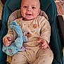 baby, infant, smiling, plush_toy, onesie, cushion, blue_seat, happy, indoor, table, flower_pattern, clothing, child, cute, portrait, person, hand, face, seat, soft_toy