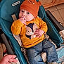 baby, child, infant, hat, orange, sweater, jeans, shoes, baby_seat, peg_perego, hand, floor, wooden_cabinet, indoor, cute, person, clothing, face, sitting, finger_in_mouth