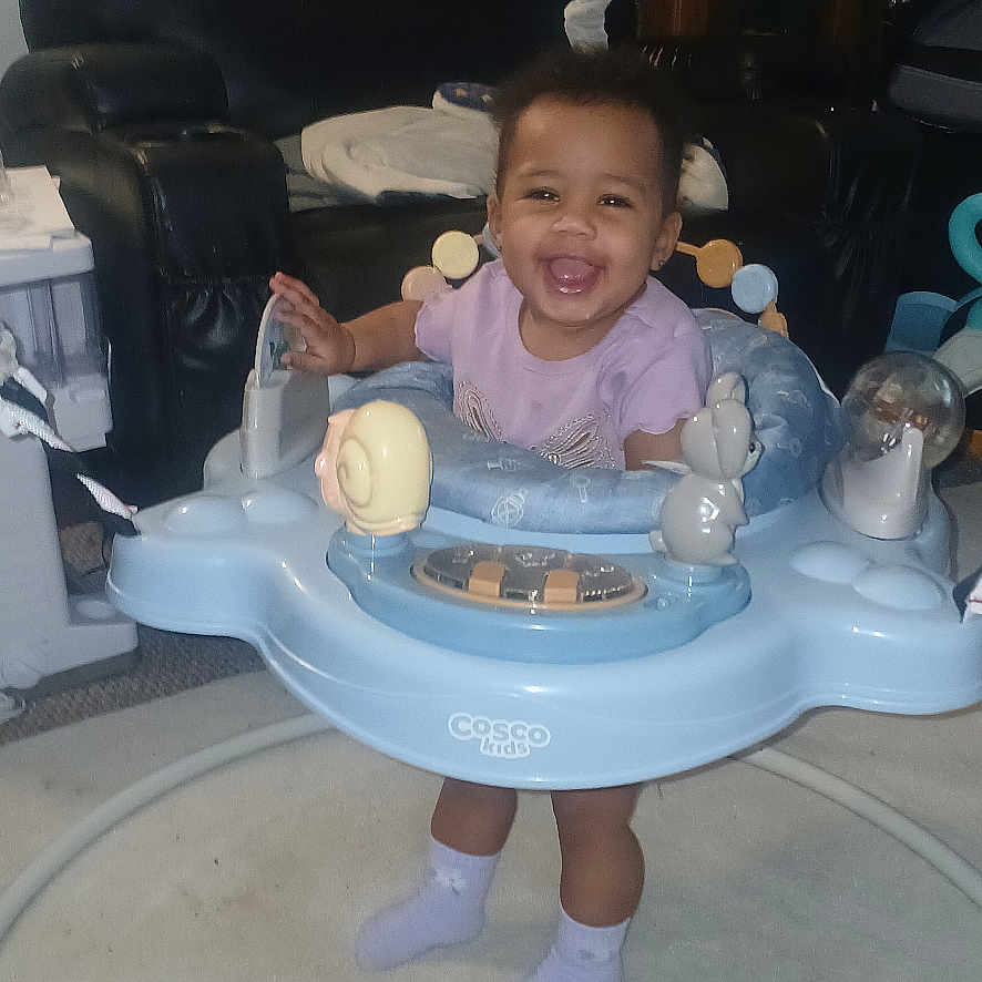 Rozariah is registered to the contest to win money with this photo: toddler, baby_walker, smiling, indoor, carpet, furniture, recliner, child, toy, socks, person, living_room, happiness, cute, playtime, home, young_child, floor, seat, entertainment