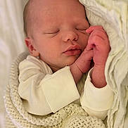 Oscar is registered to the contest to win money with this photo: newborn, baby, sleeping, blanket, knitted_blanket, infant, cozy, soft, peaceful, hands, face, closed_eyes, skin, cute, portrait, rest, warm, white_clothing, bed, comfort