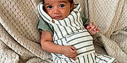 Vinnie-James is registered to the contest to win money with this photo: baby, blanket, child, cozy, cute, face, foot, green_shirt, hand, indoors, infant, person, portrait, relaxed, sitting, skin, smile, striped_overalls, texture, young
