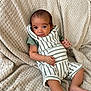 Vinnie-James is registered to the contest to win money with this photo: baby, infant, child, striped_overalls, green_shirt, blanket, texture, cute, relaxed, indoors, portrait, skin, face, smile, hand, foot, sitting, cozy, young, person