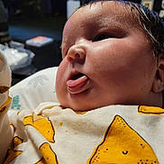 Zane is registered to the contest to win money with this photo: baby, infant, face, tongue, cute, chubby_cheeks, clothing, yellow, pattern, indoor, portrait, child, person, closeup, expression, soft_lighting, cute_outfit, smiling_pattern, newborn, cozy